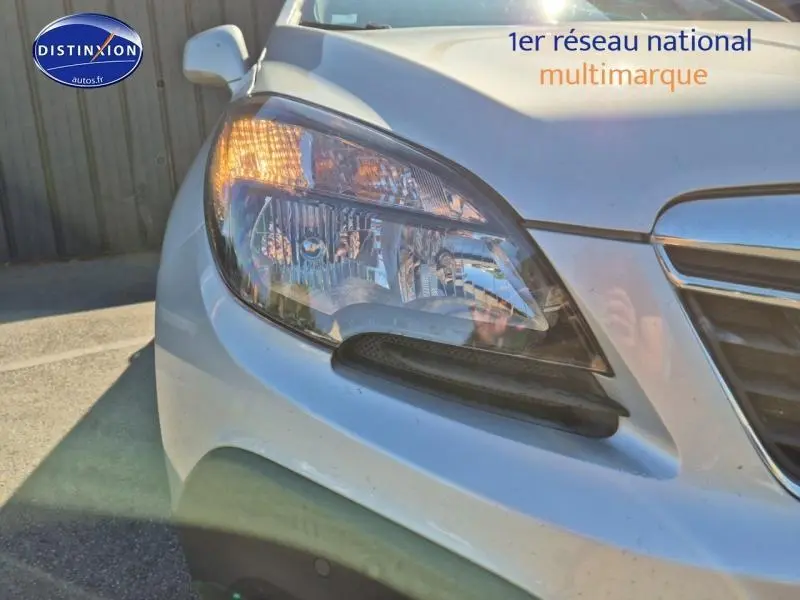 Gros plan sur le phare avant gauche d'un Opel Mokka gris Astéroïde avec calandre chromée visible.
