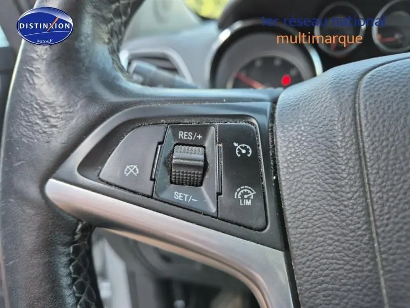 Gros plan sur les commandes de régulateur de vitesse au volant cuir noir de l'Opel Mokka gris Astéroïde, tableau de bord en arrière-plan flou.