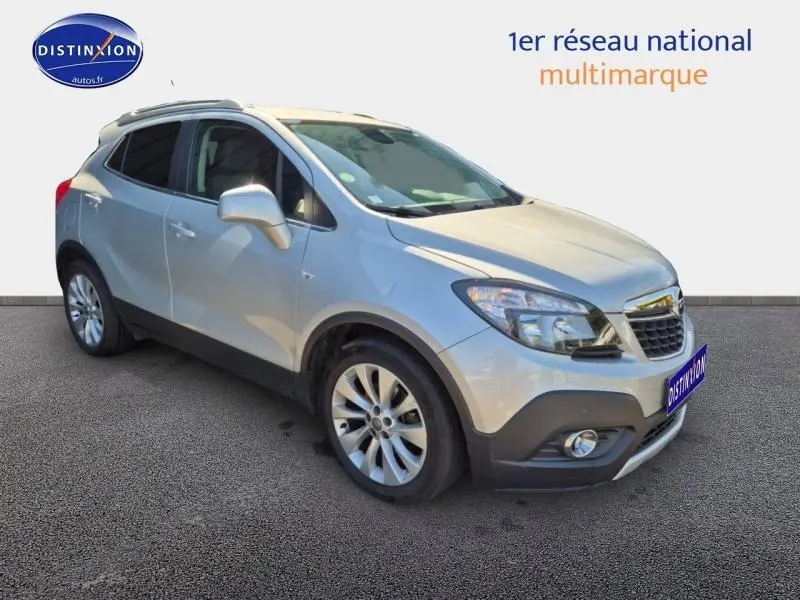 Opel Mokka gris astéroïde en vue 3/4 avant droit, avec jantes alu et barres de toit visibles.