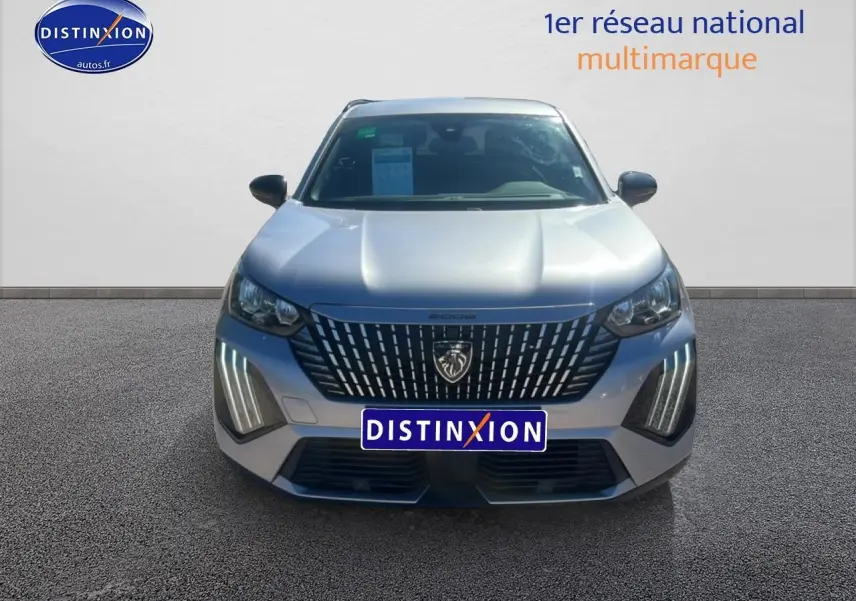 Vue frontale d'un Peugeot 2008 gris artense 2025 avec calandre distinctive et feux LED verticaux allumés.