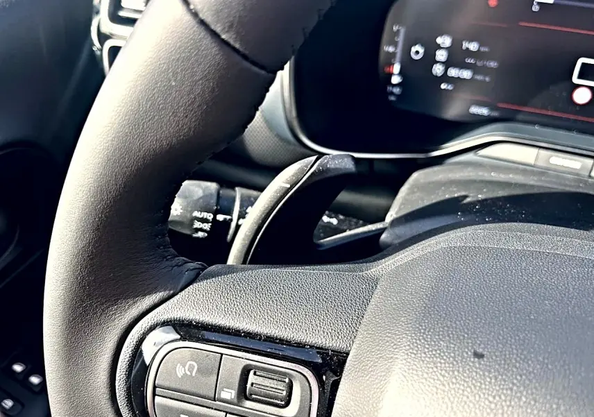 Gros plan sur le volant cuir noir du Citroën C5 Aircross 2025 avec commandes multifonctions et tableau de bord numérique flou.