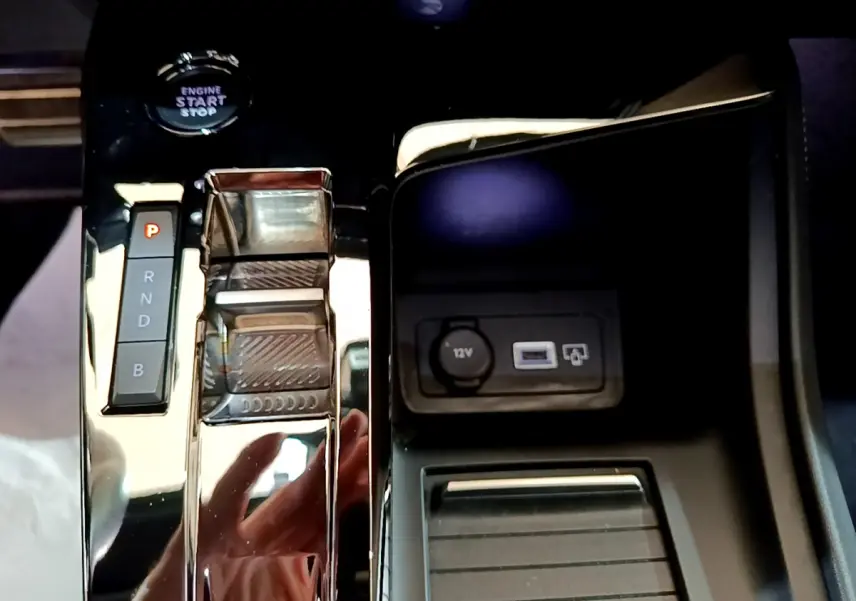 Gros plan sur la console centrale noire brillante de la Peugeot 308 PHEV 180 E-EAT8 GT avec sélecteur de boîte auto et prise 12V.