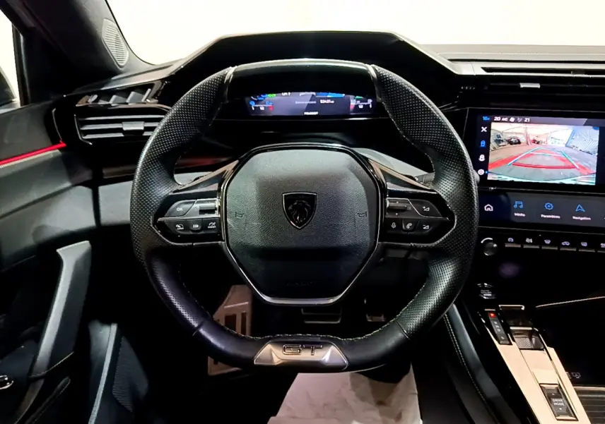 Vue intérieure centrée sur le volant cuir noir GT et tableau de bord numérique de la Peugeot 308 PHEV blanche 2022.