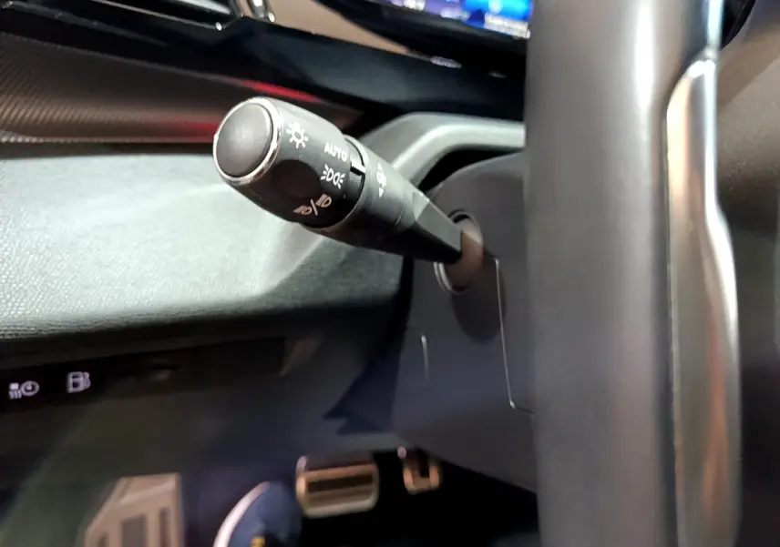 Gros plan sur la manette des phares côté gauche du volant cuir noir dans l'habitacle de la Peugeot 308 PHEV blanche 2022.