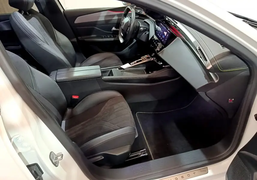 Intérieur avant droit de la Peugeot 308 PHEV 180 GT blanche, avec sièges noirs et tableau de bord digital.