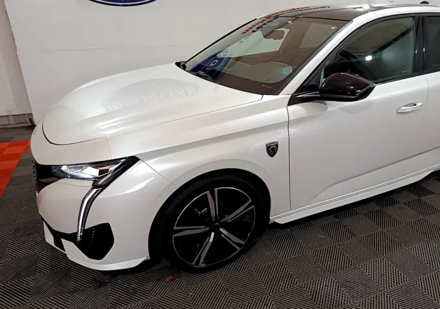 Vue 3/4 avant droit d'une Peugeot 308 PHEV 180 GT blanche avec jantes noires et logo GT sur l'aile avant.