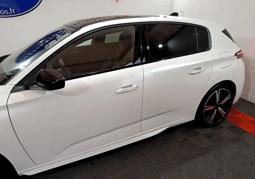 Profil droit d'une Peugeot 308 PHEV 180 E-EAT8 GT blanche avec vitres teintées et jantes noires stylisées.