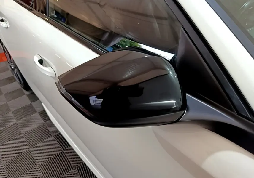 Rétroviseur noir brillant côté gauche d'une Peugeot 308 PHEV 180 E-EAT8 GT blanche vue en gros plan.