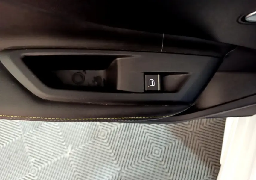 Bouton de commande de verrouillage des portes sur la garniture intérieure noire avec surpiqûres jaunes d'une Peugeot 308 PHEV 180 E-EAT8 GT blanche.