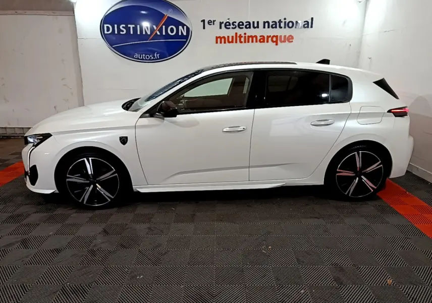 Profil côté gauche d'une Peugeot 308 PHEV 180 E-EAT8 GT blanche, avec jantes noires et logo Distinxion en arrière-plan.
