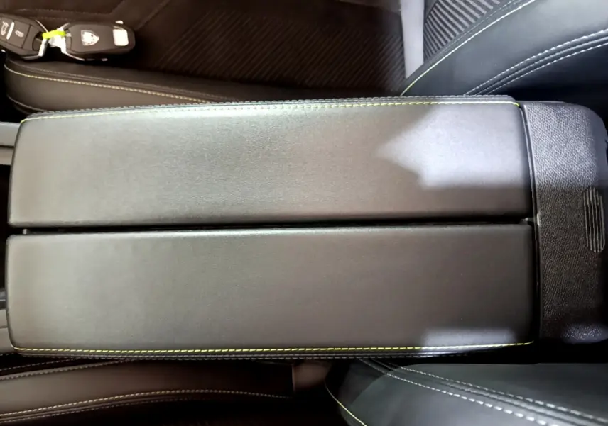 Gros plan sur l'accoudoir central noir avec surpiqûres vertes dans l'habitacle d'une Peugeot 308 PHEV 180 E-EAT8 GT.