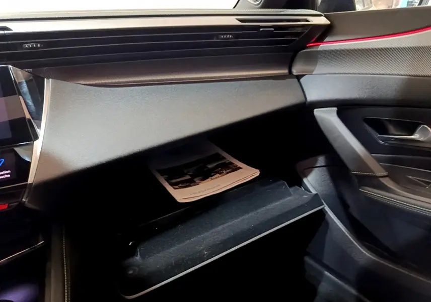 Intérieur noir de la Peugeot 308 PHEV 180 E-EAT8 GT 2022, vue sur boîte à gants ouverte côté passager avec brochure.