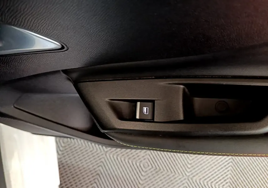 Bouton de commande de lève-vitre sur la porte intérieure noire d'une Peugeot 308 PHEV 180 E-EAT8 GT blanche.