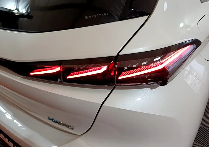 Gros plan sur le feu arrière droit allumé d'une Peugeot 308 PHEV 180 E-EAT8 GT blanche, soulignant ses lignes modernes.