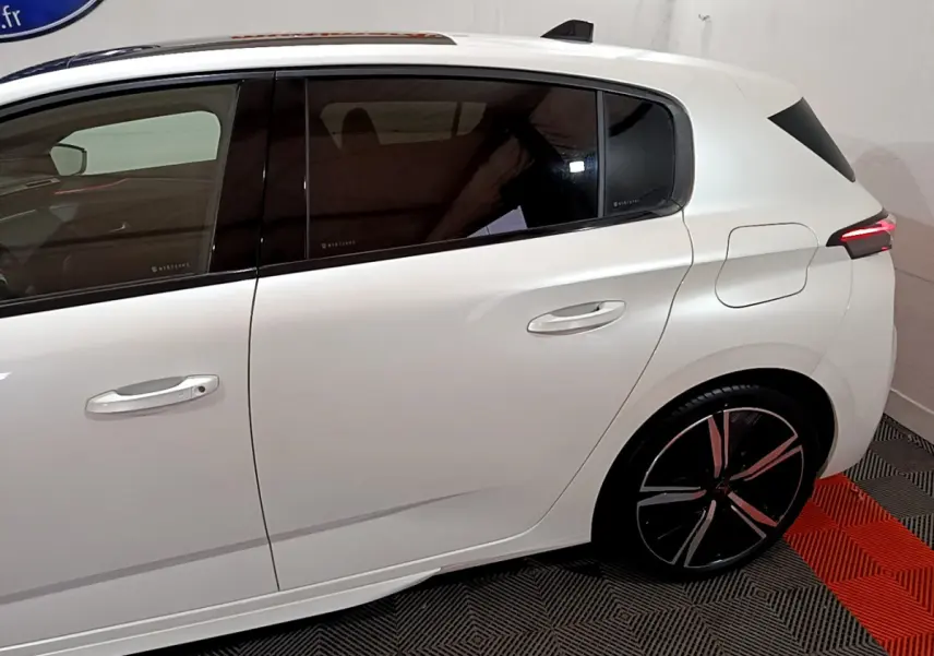 Vue latérale droite de la Peugeot 308 PHEV 180 E-EAT8 GT blanche, soulignant la porte arrière et la jante noire à motifs rouges.