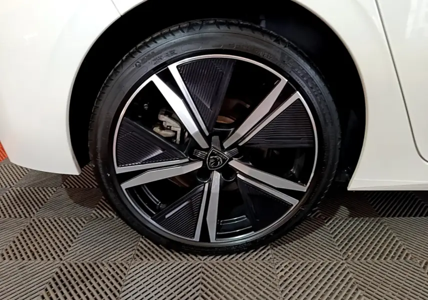 Gros plan sur la roue avant gauche de la Peugeot 308 PHEV 180 E-EAT8 GT blanche, avec jante alliage noire et argentée.