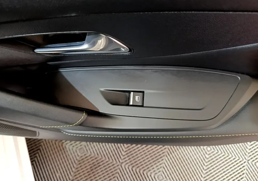 Détail de la commande de lève-vitre côté gauche sur la porte intérieure noire d'une Peugeot 308 PHEV 180 E-EAT8 GT blanche.