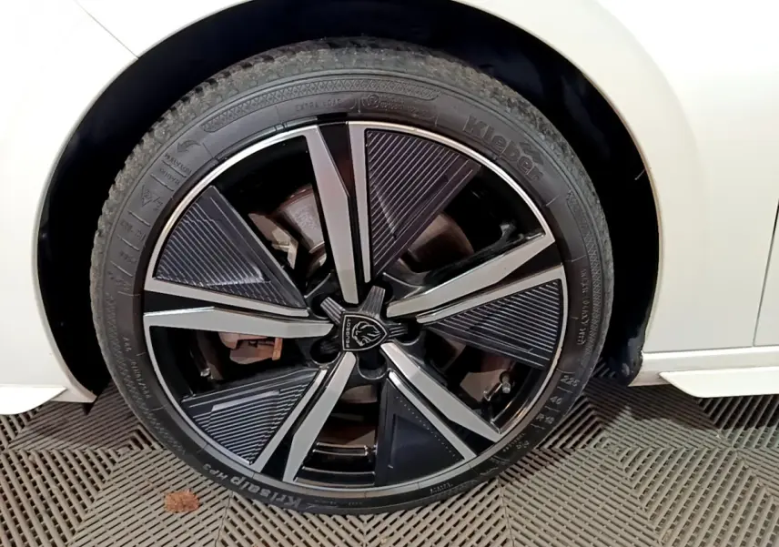 Gros plan sur la roue avant gauche d'une Peugeot 308 PHEV 180 GT blanche avec jante alliage noire et argentée.