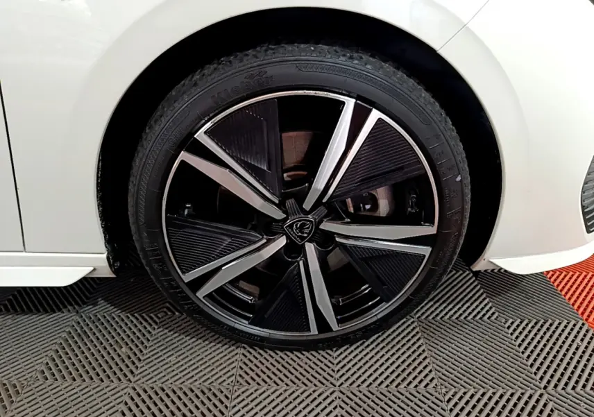 Gros plan sur la roue avant gauche de la Peugeot 308 PHEV 180 E-EAT8 GT blanche, jante alliage noire et argentée.