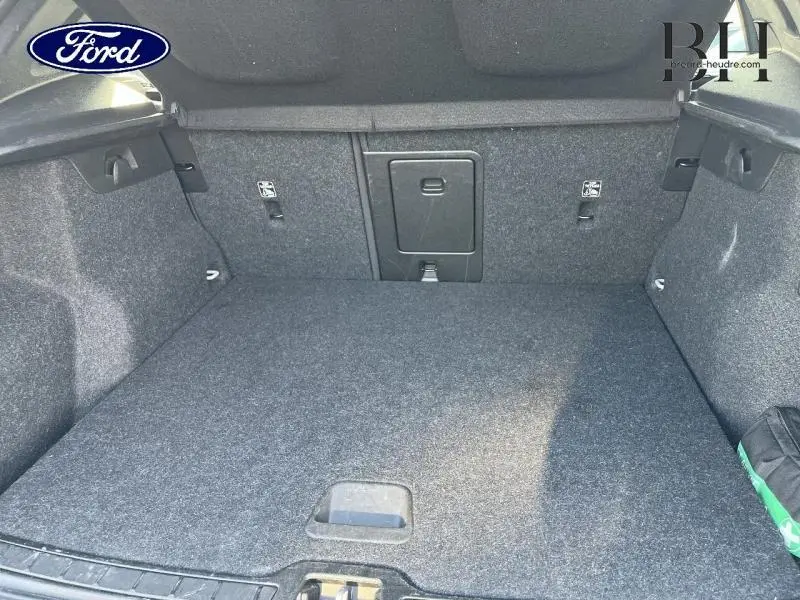 Coffre vide vu de face, revêtement gris foncé, avec trappe centrale et fixations Isofix visibles sur les côtés.