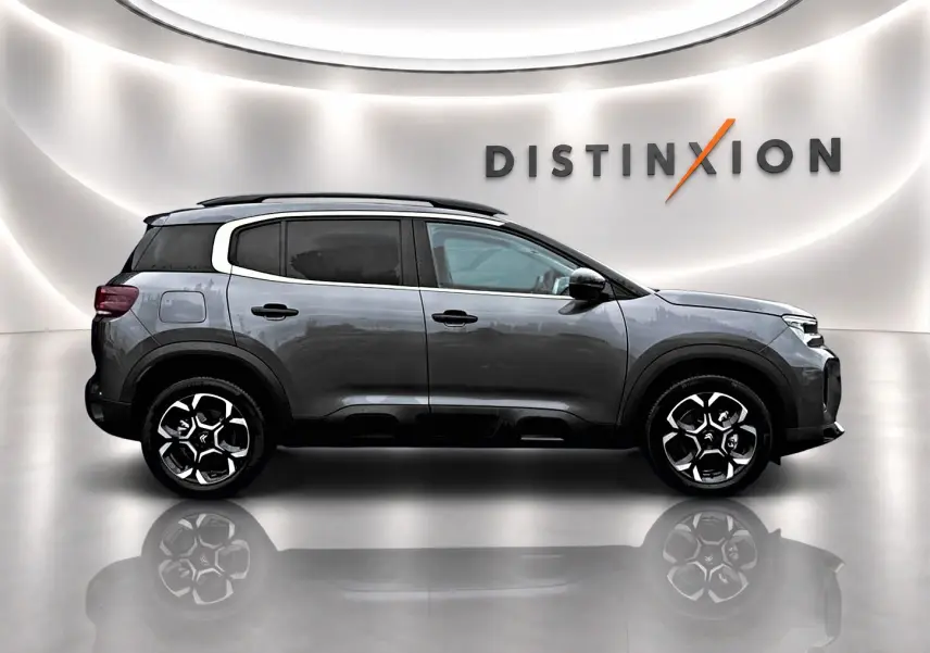 Profil droit du Citroën C5 Aircross gris platinium avec jantes alu et barres de toit, en studio lumineux avec logo Distinxion.