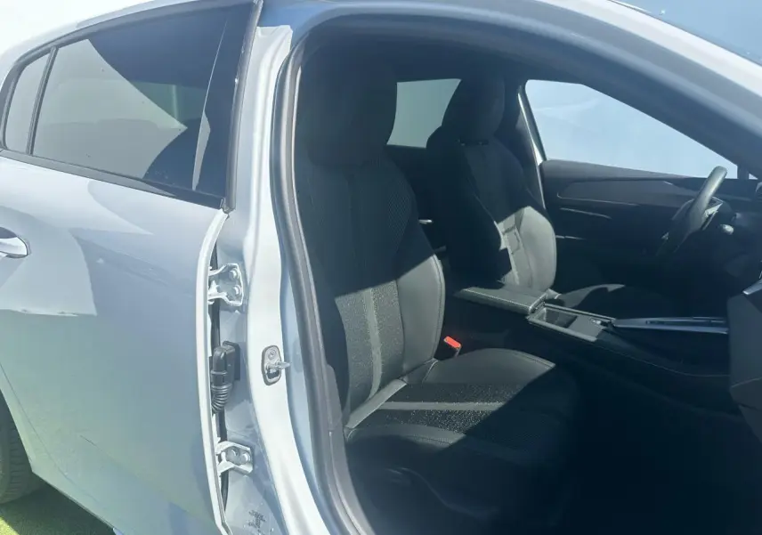 Vue côté gauche intérieur d'une Peugeot 308 blanche Okenite, sièges avant en tissu et cuir noir avec console centrale visible.