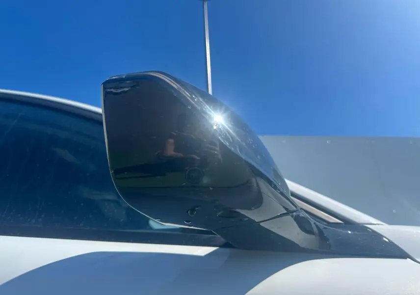 Rétroviseur droit noir brillant sur Peugeot 308 blanc Okenite sous un ciel bleu lumineux.