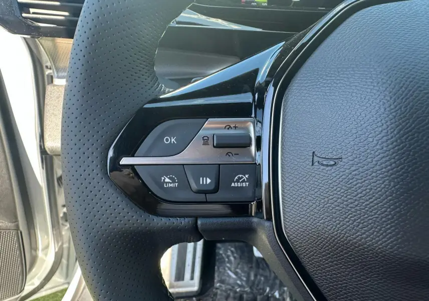 Gros plan sur le côté gauche du volant cuir perforé de la Peugeot 308 blanche avec commandes d'assistance et limitation de vitesse.