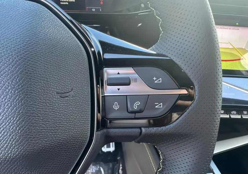 Gros plan sur les commandes du volant cuir perforé de la Peugeot 308 blanche, avec écran tactile en arrière-plan.