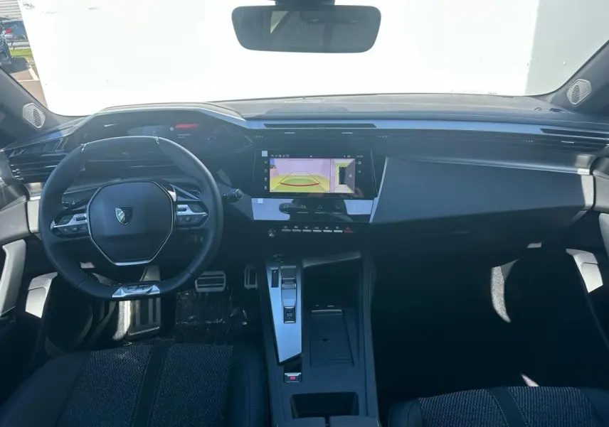 Intérieur Peugeot 308 2025 vu de face, volant compact, écran tactile central et sellerie noire moderne.