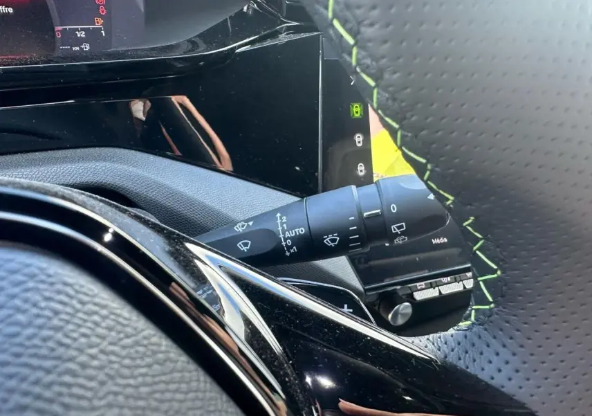 Détail du commodo d'essuie-glace et volant cuir perforé avec surpiqûres vertes dans le Peugeot 308 blanc Okenite 2025.