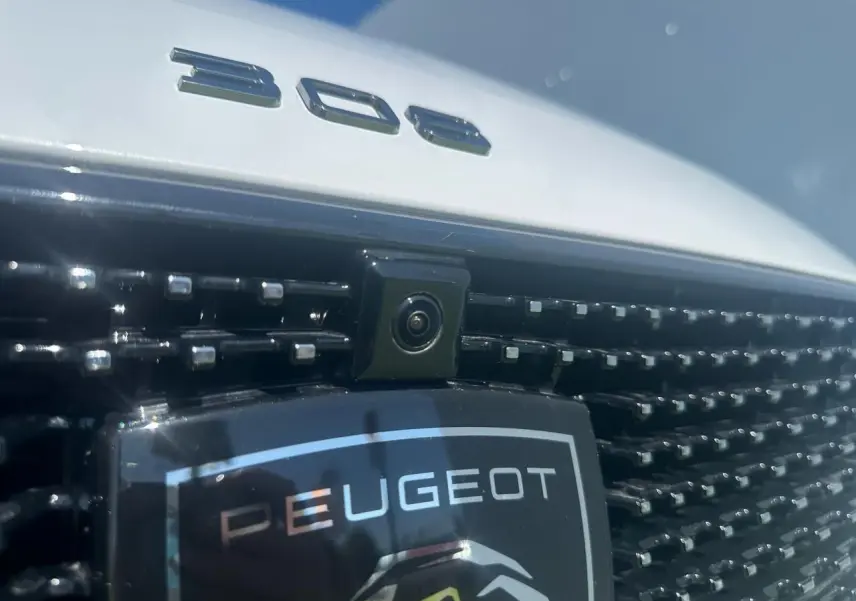 Gros plan sur la calandre noire brillante et la caméra avant d'une Peugeot 308 blanche avec logo et monogramme 308.
