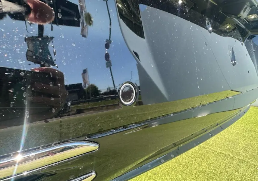 Gros plan sur le pare-chocs arrière noir brillant du Peugeot 308 blanc avec capteur de stationnement circulaire visible.