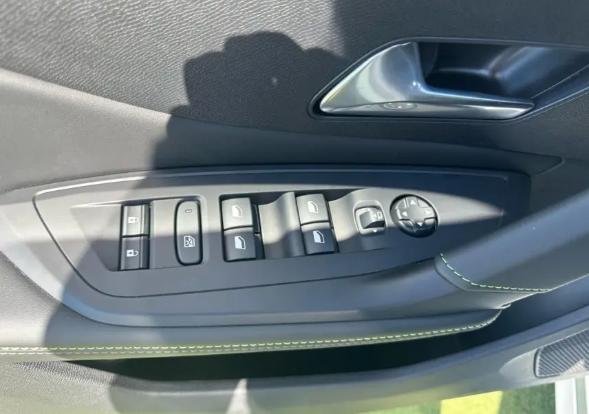 Gros plan sur la commande des vitres et rétroviseurs côté gauche, garniture noire avec surpiqûres vertes.