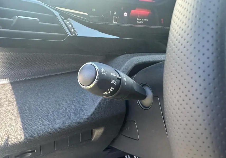 Gros plan sur la commande des feux à gauche du volant perforé dans l'habitacle noir de la Peugeot 308 2025.