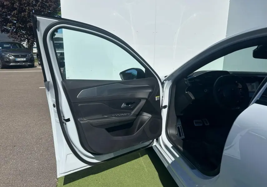 Portière avant gauche ouverte d'une Peugeot 308 blanche, montrant l'intérieur noir et le tableau de bord partiel.