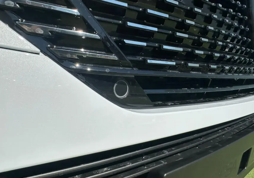 Gros plan sur la calandre noire brillante et la partie avant blanche nacrée d'une Peugeot 308 2025.