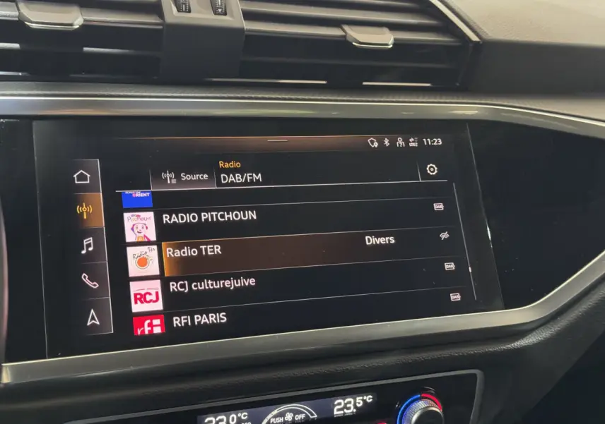 Écran tactile central de l’Audi Q3 noir 2022 affichant les stations radio DAB/FM avec commandes climatisation digitales.