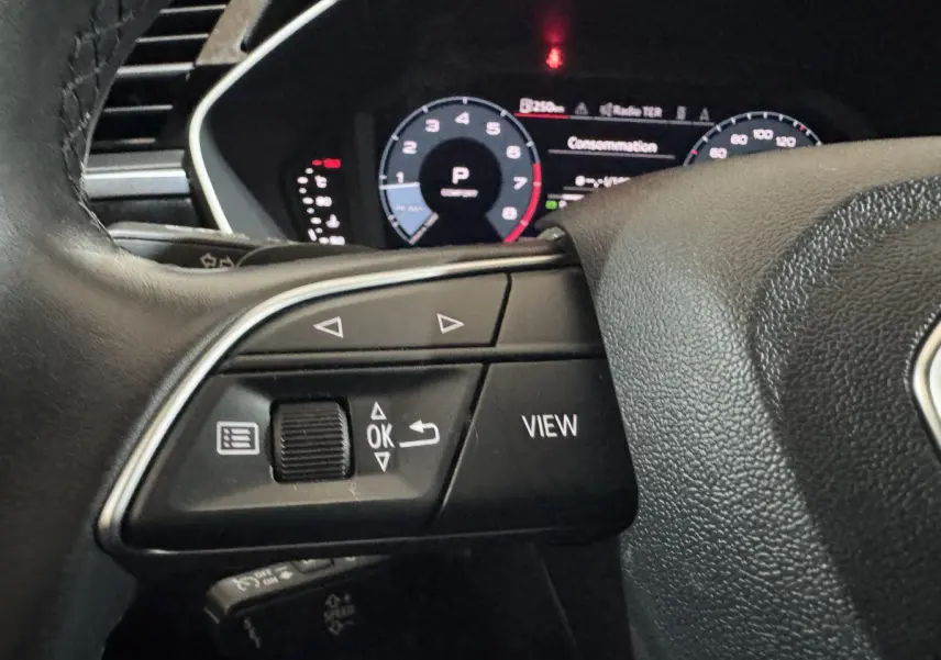 Gros plan sur les commandes gauche du volant noir d’un Audi Q3 35 TFSI 2022 avec tableau de bord numérique en arrière-plan.