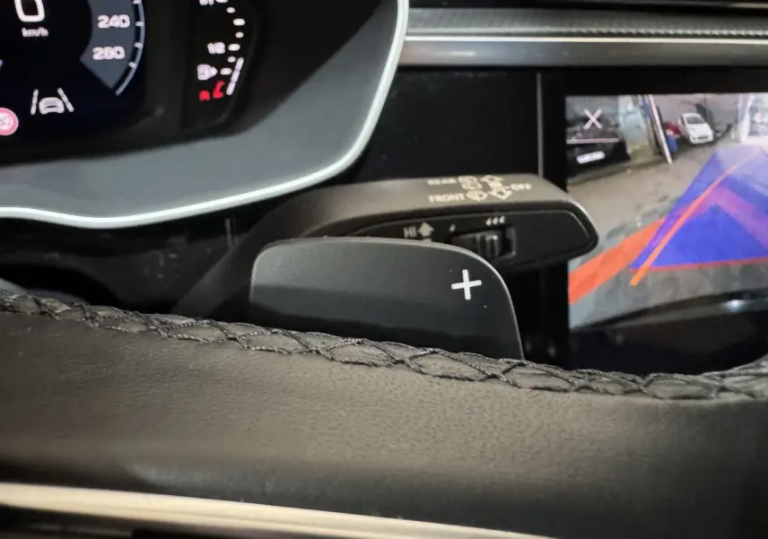 Gros plan sur la palette de changement de vitesse droite du volant cuir noir d’un Audi Q3, avec affichage caméra de recul visible.