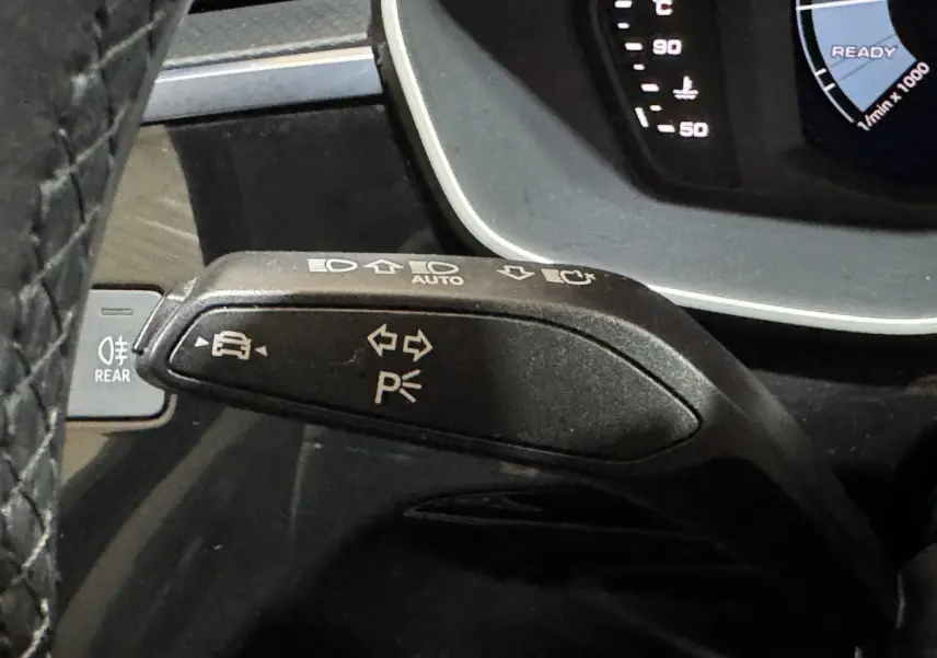 Gros plan sur la manette de clignotant noire de l'Audi Q3 35 TFSI, avec tableau de bord numérique partiel visible.