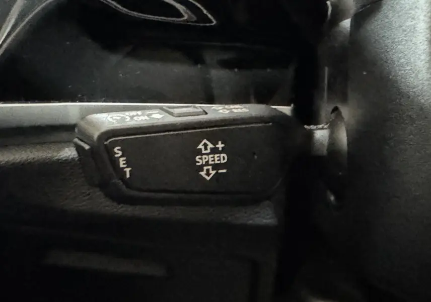 Gros plan sur la commande de régulateur de vitesse noir dans l’Audi Q3 35 TFSI 2022, intérieur sombre.