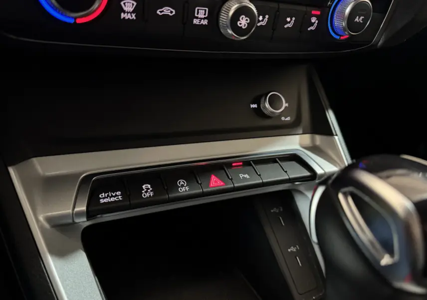 Gros plan sur la console centrale de l'Audi Q3 35 TFSI noire, montrant les boutons de contrôle et la molette de réglage.
