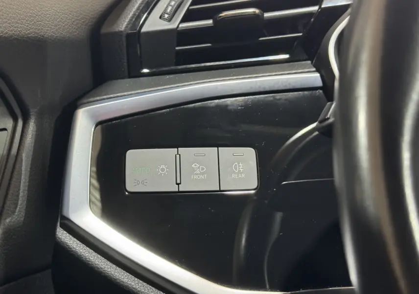 Détail des commandes d’éclairage sur panneau noir brillant côté gauche du volant d’un Audi Q3 noir 2022.