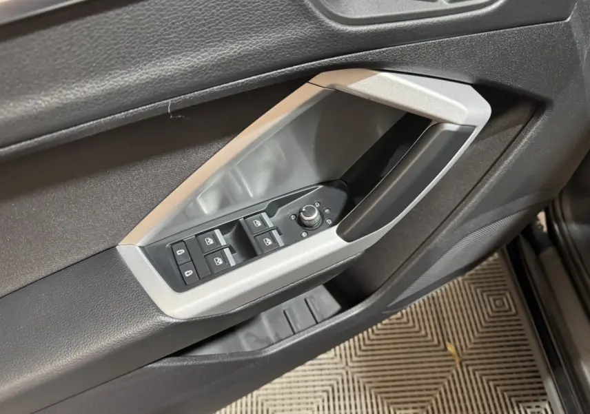 Gros plan sur la commande des vitres et rétroviseurs côté conducteur de l'Audi Q3 noir, avec cadre argenté.