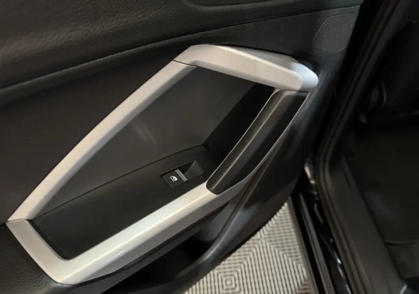 Gros plan sur la poignée intérieure côté gauche de la porte noire d’un Audi Q3 35 TFSI 2022 avec bouton de commande de vitre.