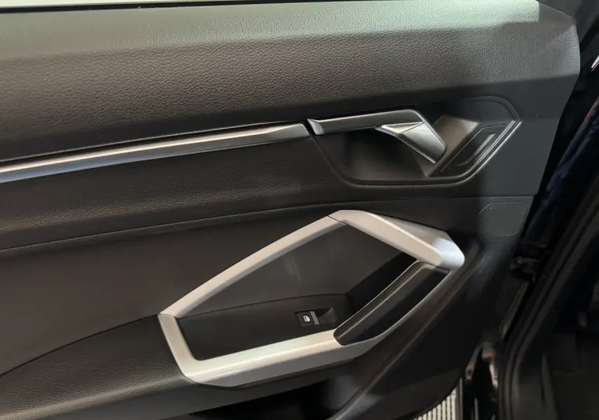 Vue rapprochée de la porte avant droite noire de l'Audi Q3 35 TFSI 2022 avec poignée argentée et bouton de verrouillage.