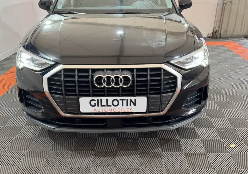 Vue avant d’un Audi Q3 noir 2022 avec calandre hexagonale et phares LED allumés dans un garage.