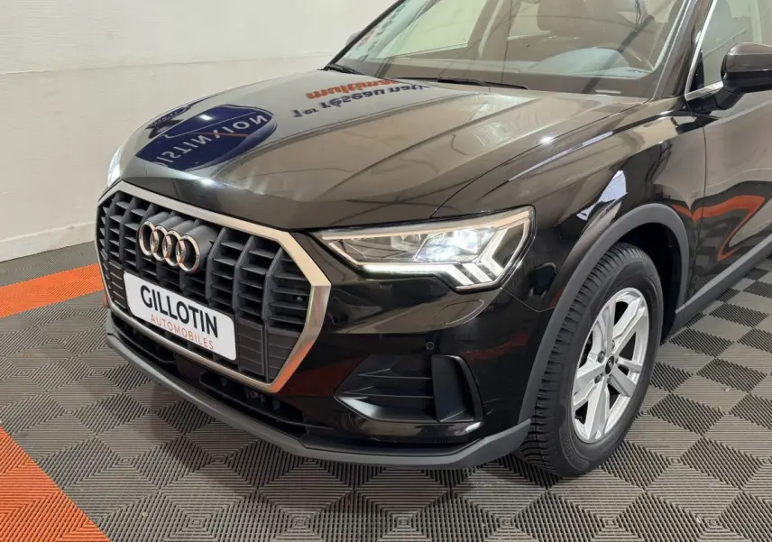 Vue 3/4 avant droit d'un Audi Q3 noir avec calandre hexagonale et phares LED allumés en intérieur showroom.