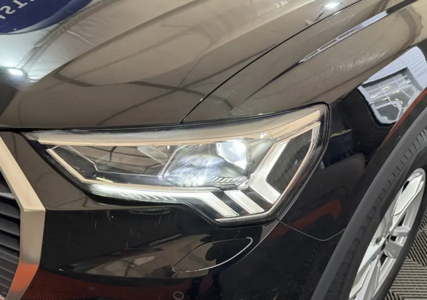 Gros plan sur le phare avant droit LED d’un Audi Q3 noir 2022, mettant en valeur ses lignes anguleuses et la jante alu visible.
